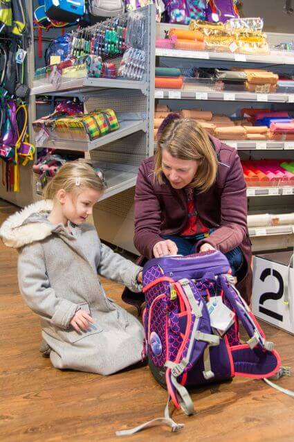 Eine Mutter und ihr Kind sind für eine Schulranzenberatung in einem Schulranzen-Fachgeschäft. Gemeinsam sitzen sie vor einem Schulranzen der Marke ergobag und schauen sich ihn näher an.