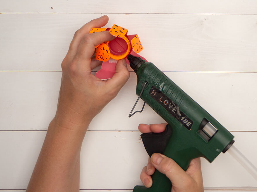 Jemand klebt das angemalte Oberteil einer kleinen Plastikflasche in das, zu einer Blume geformten, Unterteil der Plastikflasche. Der Untergrund ist hell. Foto: Johanna Rundel