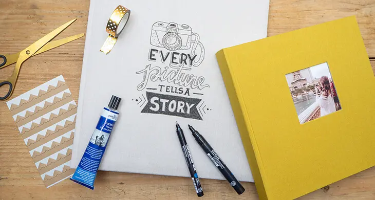 Auf einem rustikalen Holztisch liegen verschiedene Fotoalben aus Leinen von Goldbuch, sowie Materialien zur Gestaltung des Deckblatts. Foto: Johanna Rundel