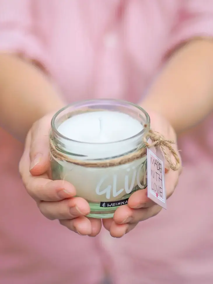 Zwei Hände halten eine selbstgemachte Kerze im Glas in die Kamera