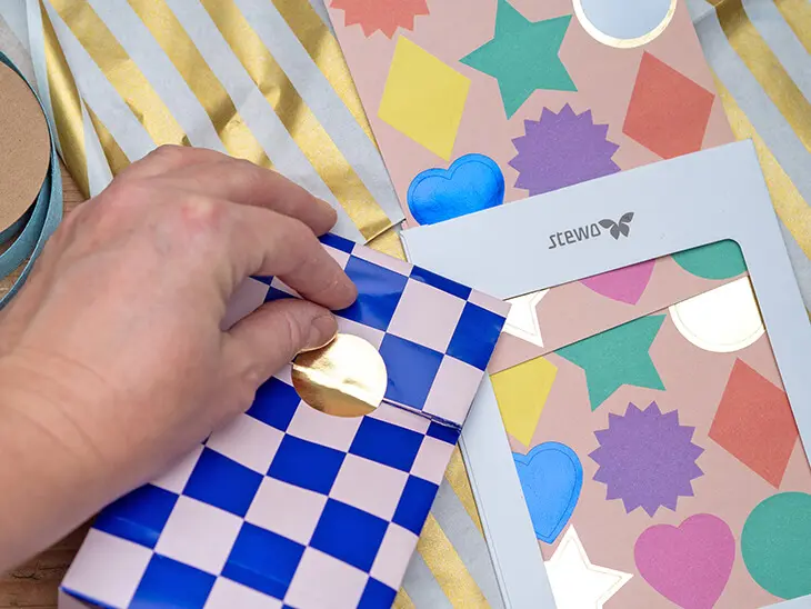 (jemand klebt einen Aufkleber von STEWO auf eine selbstgebastelte Geschenktüte. Foto: Johanna Rundel