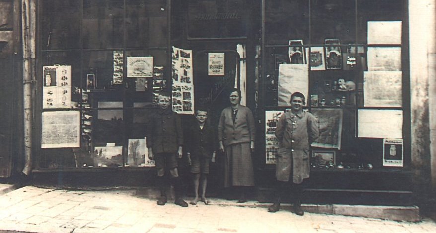 Eine Familie, bestehend aus zwei Erwachsenen und zwei Kindern, steht vor der Ladenfront von Zauner im Jahr 1910.