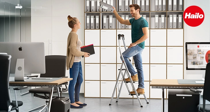 Mitarbeiter nutzt eine Hailo Stehleiter im Büro bei Montagearbeiten