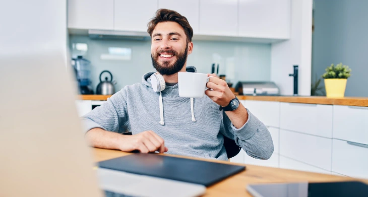 Mann im Homeoffice mit Laptop und Kaffeetasse am Küchentisch.